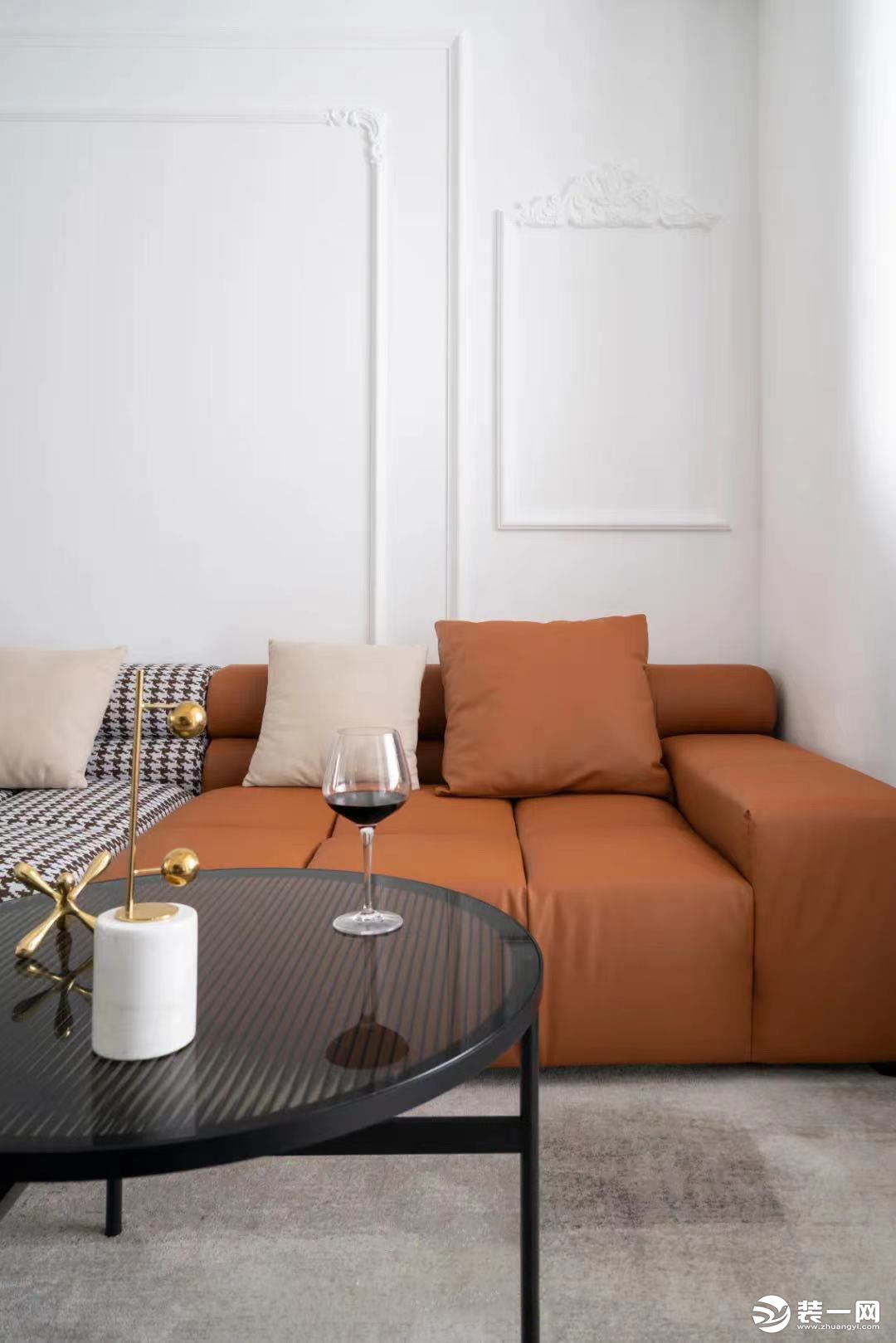以纯白为基调的空间里，咖色千鸟格与爱马仕橙组合沙发成为客厅的视觉焦点，与阳台角落里的蓝色柜体形成不动