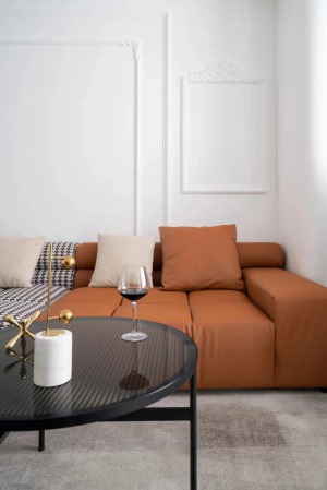以纯白为基调的空间里，咖色千鸟格与爱马仕橙组合沙发成为客厅的视觉焦点，与阳台角落里的蓝色柜体形成不动