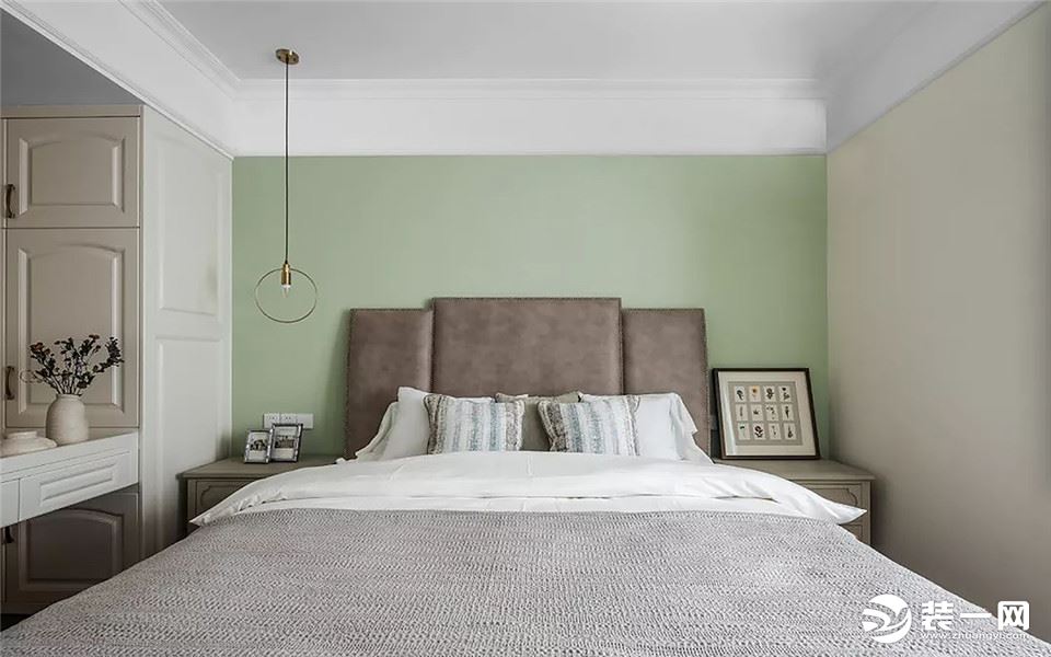 卧室床头墙以草绿色为背景，搭配一张皮艺靠背床，还有一盏圆环铜艺灯，布置出一个轻松自然的睡眠空间