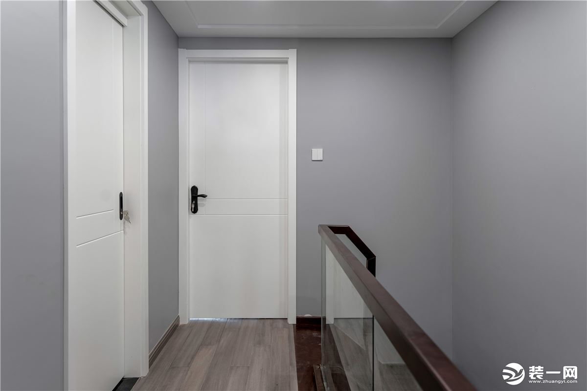 顺楼梯上楼，纯灰色墙面、原木地板和白色木门在视觉上营造了简约清爽的视觉效果。