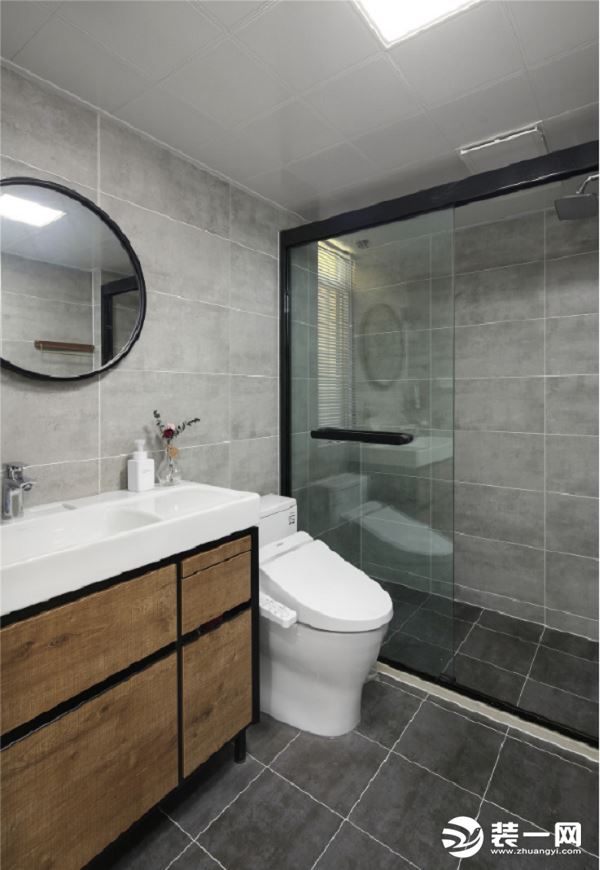 灰色的墙面和地面砖搭配木色的浴室柜，透明的玻璃作为干湿分断的隔离，镜子采用圆形状，不同于方正的镜子，