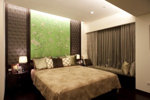 卧室的设计有着独特的新古典式的风格，床头木质雕花与绿色背景墙面极富装饰性，红木地板增添了几分温暖，绸