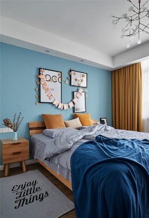 木质地板舒适温暖，灰色床品与地毯，深蓝色的毛毯舒适惬意，淡蓝色的床头背景和几幅简单的挂画，枝蔓状的灯