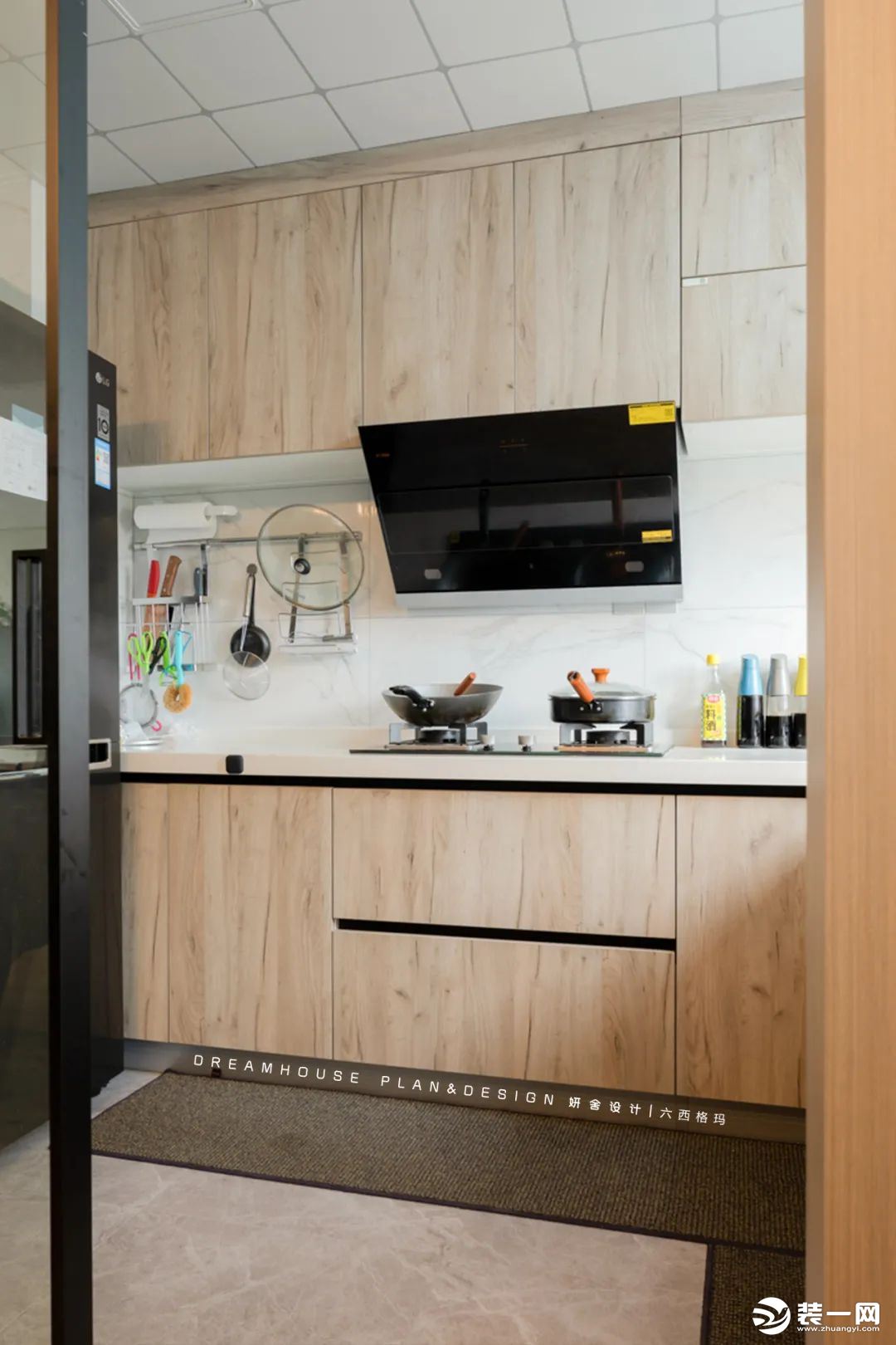 黑色大冰箱摆放在了厨房的一侧，以灰色地砖搭配木色橱柜，过渡到白色台面和墙砖，打造出一个简洁明快的烹饪