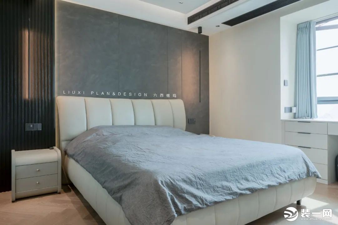床头背景墙使用了黑色长城板+线性吊灯、水泥灰墙板拉槽硬包装饰，勾勒出毫不单调的床头景观。暖白色的床搭