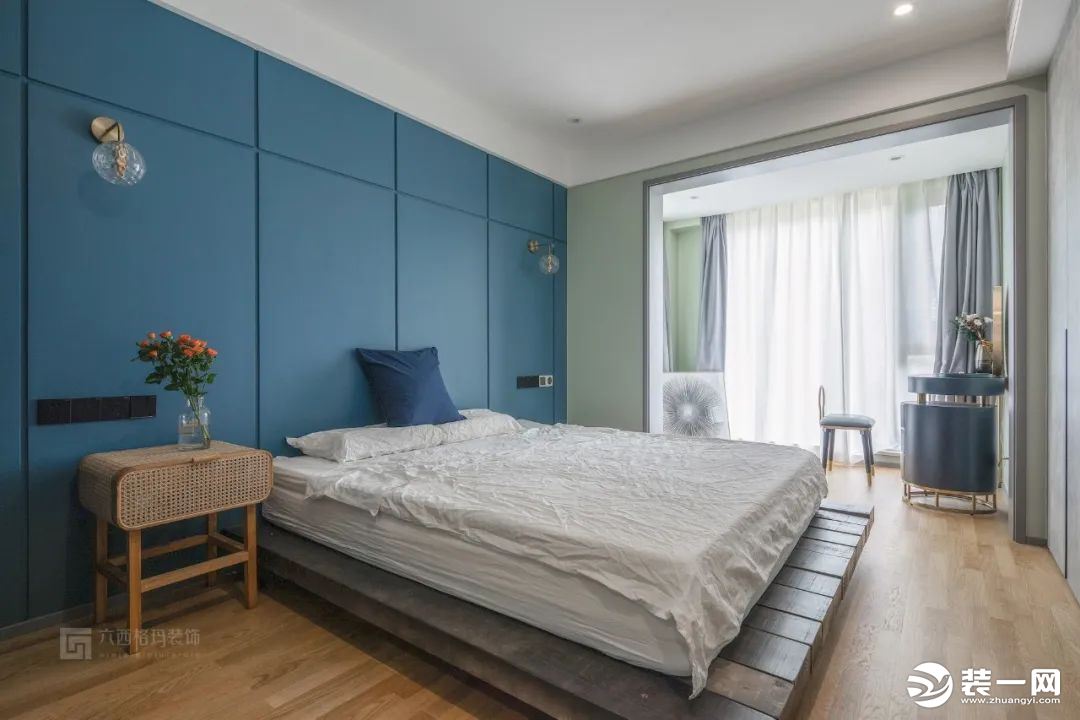 床头背景墙采用石膏板拉缝工艺涂刷深海蓝艺术漆，造型简洁却极具设计感。床对面是一整排定制的大衣柜，水泥