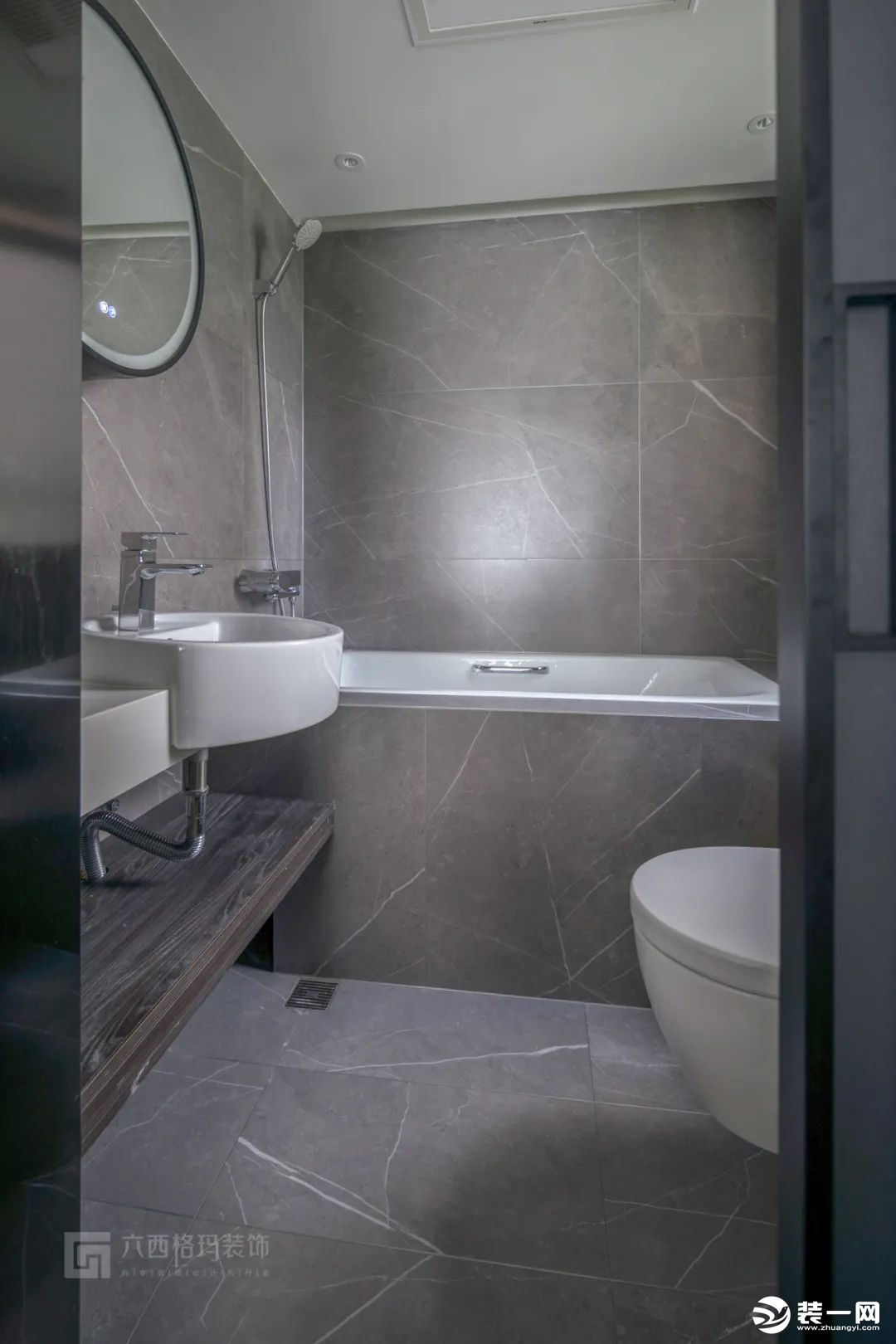 主卫墙地面铺贴600*1200的灰色大砖，搭配简洁的浴室柜。顶面使用防水石膏板，浴缸靠边，马桶和洗手