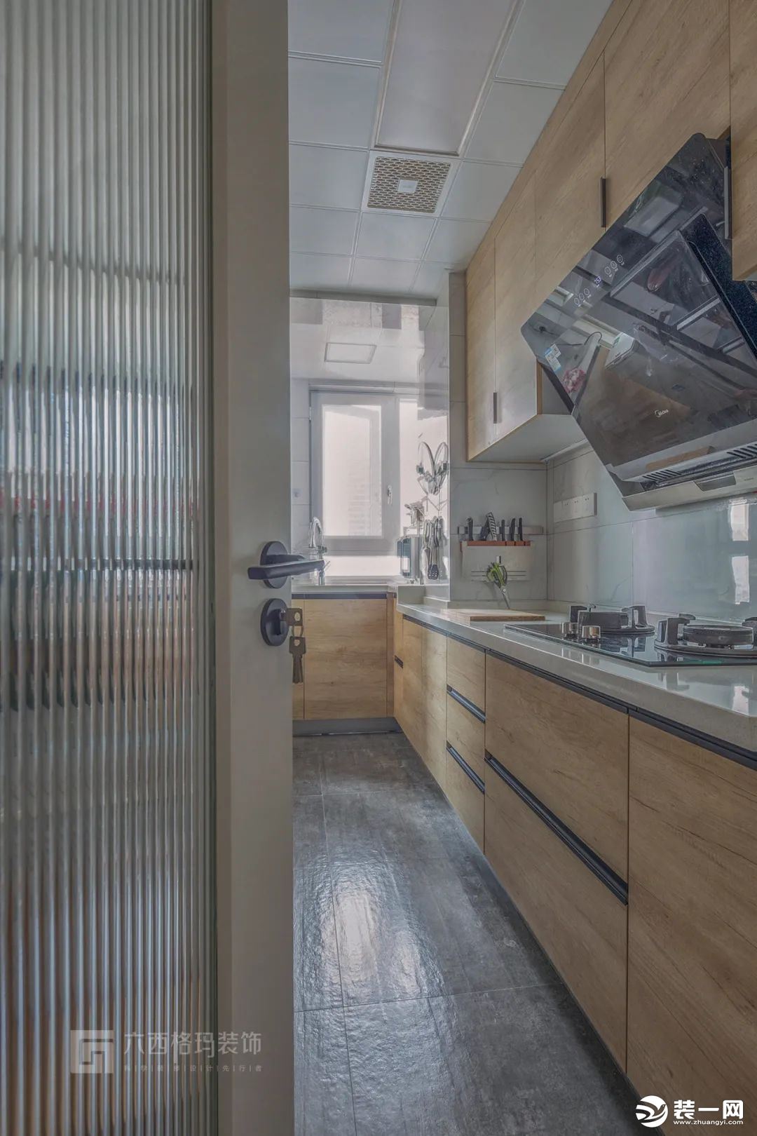 廚房以網紅款的長虹玻璃門，搭配灰黑色地磚，顯得簡約端莊。木色的櫥柜，白色的操作臺面，展現出簡約風的美