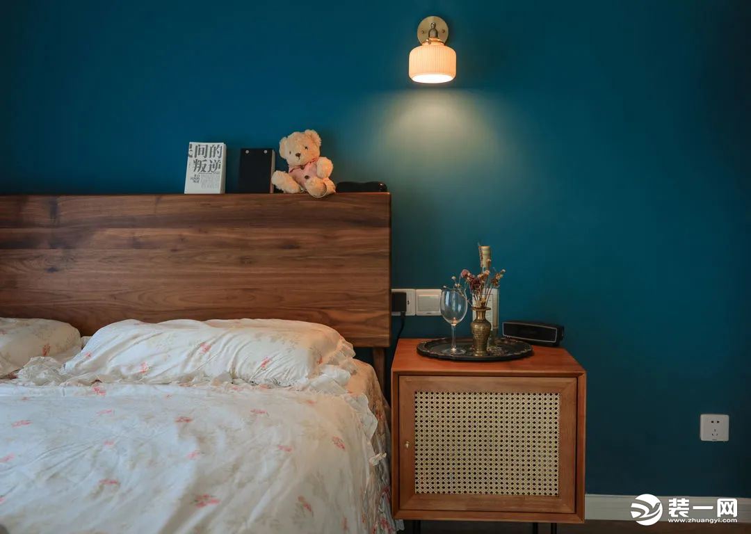 卧室刷了一面更深更静谧的蓝色，胡桃木床头板有一定宽度可以放些睡前读物。藤编门的床头桌和玄关柜呼应，屋