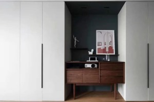 在衣柜和陈列柜中间是定制的胡桃木斗柜，墙漆颜色和沙发墙形成呼应，一直延伸至顶面，让这个小空间更具有完