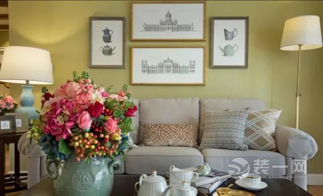 金色边框的装饰画和奶咖绿的墙面，搭配大地色系的抱枕，一切都是那么的和谐，与鲜艳的花艺构成一幅美丽的画